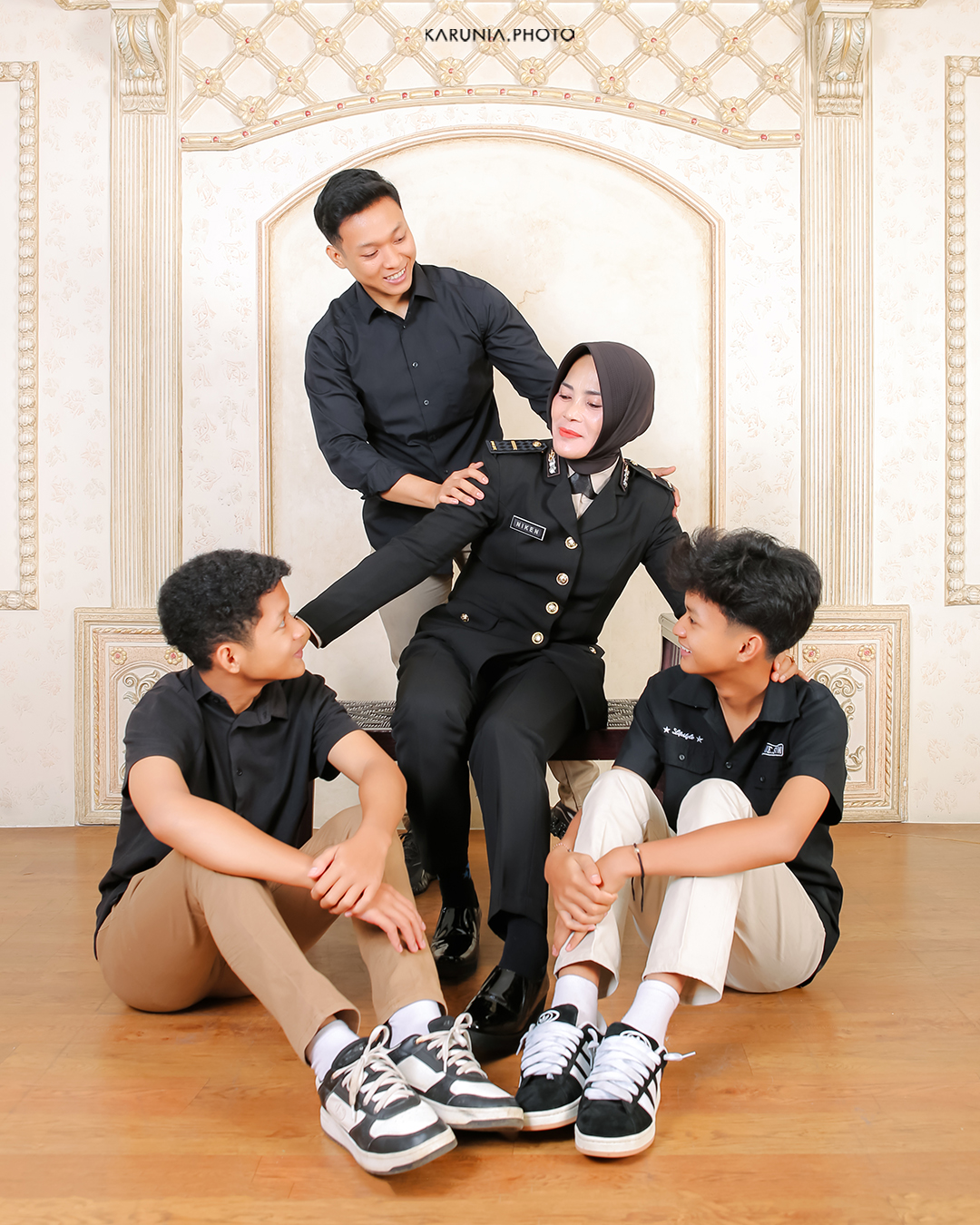Three siblings sitting on wooden steps in coordinating outfits with genuine smiles and relaxed poses